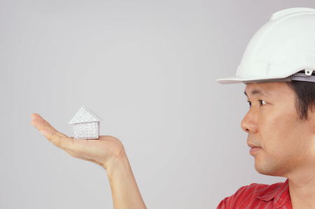 Engineer wear red shirt and white engineer hat is looking at house on hand with white background.の写真素材