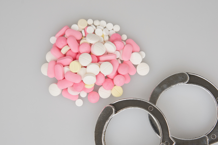 Silver handcuffs and stack of tablets place on white background.の写真素材