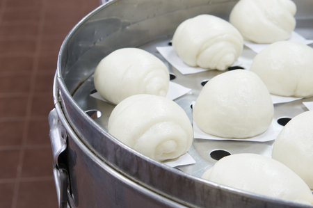 Steamed bun or dim sum on white paper in big aluminium steamer at restaurant kitchen with brown tile on floor as background and copy space. Food and healthy concept photography.の写真素材