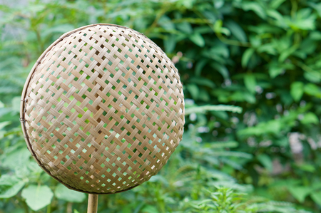 Brown wicker bamboo basket hanging on bamboo stick have blur green leaves as background with copy space.の写真素材