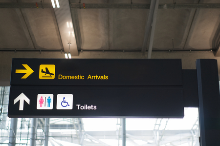 Domestic arrivals and toilets information board sign with yellow and white character on black background at international airport terminal.の写真素材