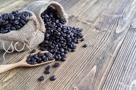 Close up stack of coffee bean on wooden spoon and in brown sack place on wooden background with copy space. Coffee bean full of sack as abundant. Food and drink concepts.の写真素材