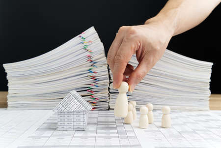 Man is laying boss wooden doll near house with employees have blur overload financial report of sale with black background and copy space. Business and finance concept leadership vision successfully.の写真素材