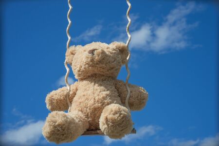 teddybear playing on a swing with the blue sky backgroundの写真素材