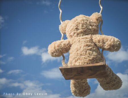teddybear playing on a swing with the blue sky backgroundの写真素材
