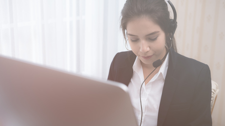 Young beautiful girl working at a laptop in a small medium enterprise. She is operating the phones and computerの写真素材