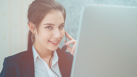 Young beautiful girl working at a laptop in a small medium enterprise. She is operating the phones and computerの写真素材