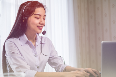 Young beautiful girl working at a laptop in a small medium enterprise. She is operating the phones and computerの写真素材