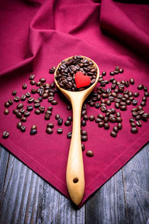 coffee bean and heart in wooden ladle on red napkin top of wood tableの写真素材