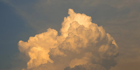 A magnificent view of large cumulus clouds dramatically illuminated with warm, golden light from the setting sun, creating a majestic and glowing sky.の写真素材
