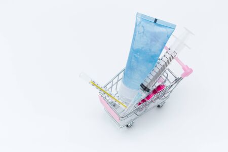 Medical equipment in small shopping trolley, sanitizer gel syringe thermometer and medicine on white background.の写真素材