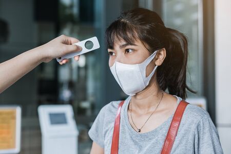 Officer checking fever with digital thermometer visitor asian woman before entering the building,...