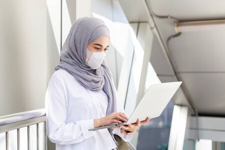 Asian muslim businesswoman wearing medical mask for prevent dust and infection virus working with laptop on the way go to office.の写真素材
