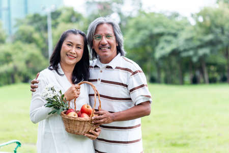 happy asian senior couple holding basket apple and flower picnic in public park.の写真素材