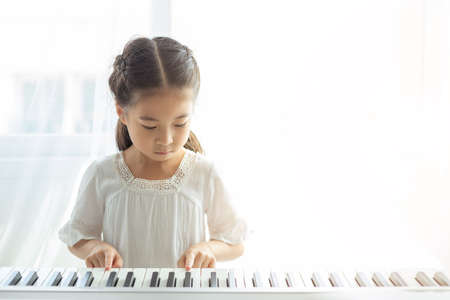 asian beautiful child girl playing electric piano in living room at home.の写真素材