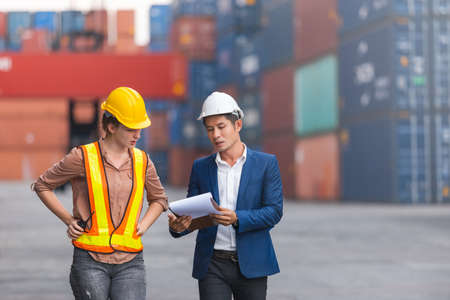 Asian foreman holding clipboard and engineering women work at  containers in cargo ship for import...