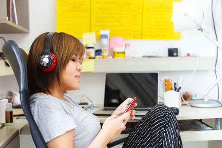 asian woman wearing headphone using mobile phone work at home.