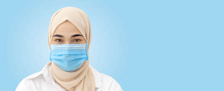 close up face muslim woman wearing medical mask for prevent infection virus on blue background.の写真素材