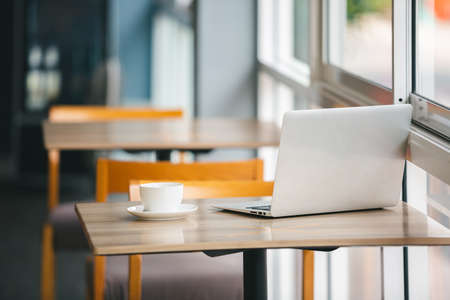 Laptop computer and white coffee cup on wooden table in coffee shop. Relax work time.
