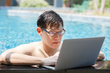 asian businessman working with laptop in swimming pool. work new normal. lifestyle travel in holiday vacation. relaxation concept.の写真素材