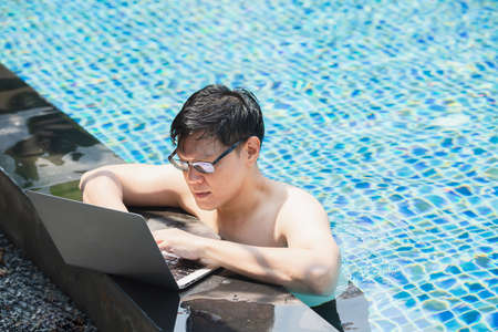 asian businessman working with laptop in swimming pool. work new normal. lifestyle travel in holiday vacation. relaxation concept.の写真素材