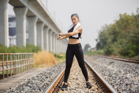 Asian young woman tan skin in black sportswear outdoor physical exercises for successfull health at railway side and eye contact to camera.の写真素材