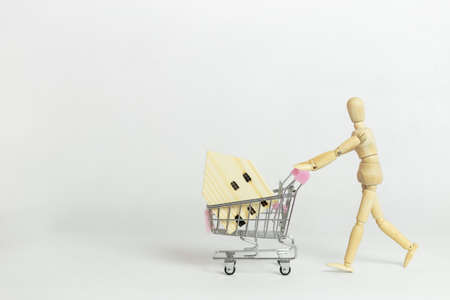 Wooden mannequin or puppet pushing shopping cart with wooden house on white background, business sale and purchase property concept.の写真素材