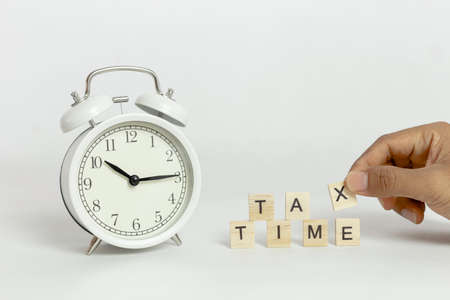 White alarm clock with handing tax wooden block cube on white background.の写真素材