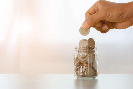 coins in glass bottle put on table with hand putting money coins, save or investment concept.の写真素材