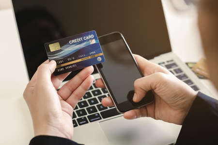 Close up hand woman holding credit card and using smartphone with laptop at home. online buying or...