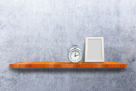 Empty photo wood frame and alarm clock on put on wood shelves with concrete wall background.