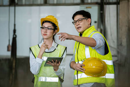 asian men and women engineer worker standing at factory talk about project with her uses digital...