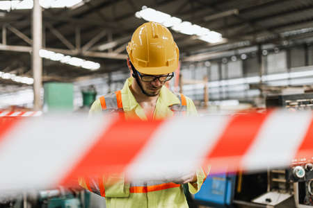 Industrial man wearing uniform safety and helmet in factory blurred foreground, space barrier tape safety zone.の写真素材