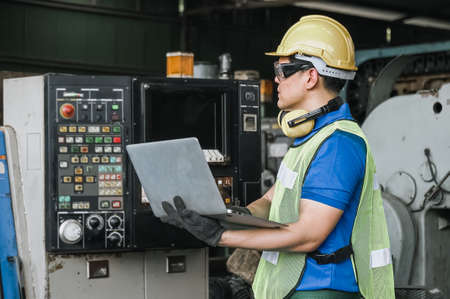 man Industrial engineers wearing safety uniform and hard hats with laptop working heavy industry in factory.の写真素材