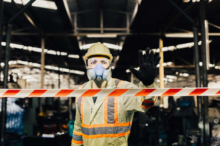 Man engineer wearing safety uniform with gloves and gas mask show hand signal stop in dangerous area, don't enter.の写真素材