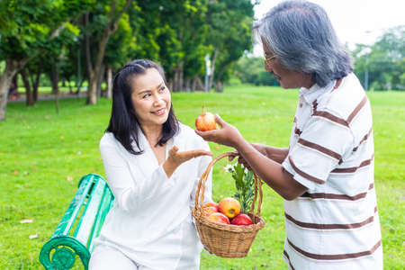 Happy senior couple with apple in basket sitting in the garden.の写真素材
