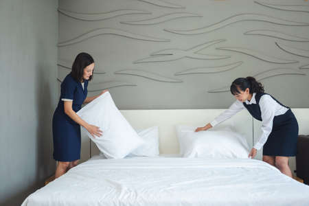 Asian young woman room maid making bed and pillow in hotel. staff bedroom hotel service.の写真素材
