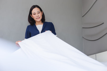 asian young woman room maid making arrange bed pillow in hotel. staff bedroom arranging cleaning of hotel.の写真素材