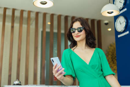 Beautiful tourist woman standing using smartphone at front counter check in of hotel.の写真素材