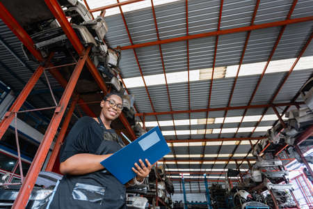 African american worker woman wear spectacles crossed arms holding clipboard standing in factory auto parts. female employee business warehouse motor vehicle.の写真素材