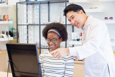 asian man professional optician selling and young woman african american choosing spectacles glasses âin optician store. used correct assist defective eyesight.の写真素材