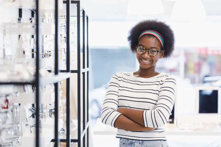 portrait young woman African american afro hair smile and crossed hands wear spectacles standing at in optical shop. modern ophthalmologist concept.の写真素材