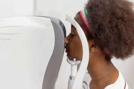Close up face of young woman african american examining eyesight modern machine equipment in clinic....