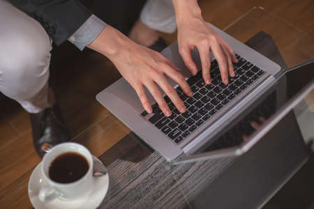 Top view, close up businessman hands using laptop working at office with coffee cup on glass table.