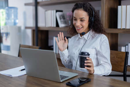 Beautiful woman wearing headset sitting at table hand motion having conversation online with laptop...