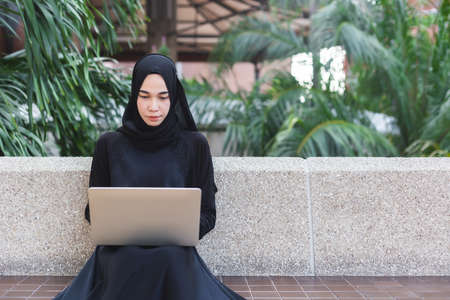 Muslim woman in black hijab working with laptop outdoor office.