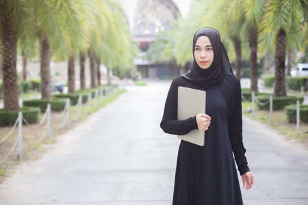 Portrait muslim woman in black hijab with laptop nature background.の写真素材