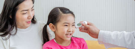 Patient little girl are checking for fever with a thermometer and mother sitting together, doctor is using a thermometer. Temperature measurement In little girl body.の写真素材