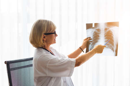 senior woman doctor examining x-ray report in medical hospital.