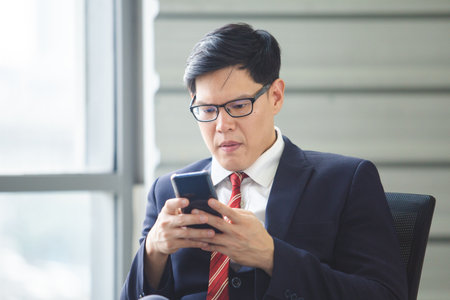 asian businessman sitting using smartphone telephone online working in office.の写真素材